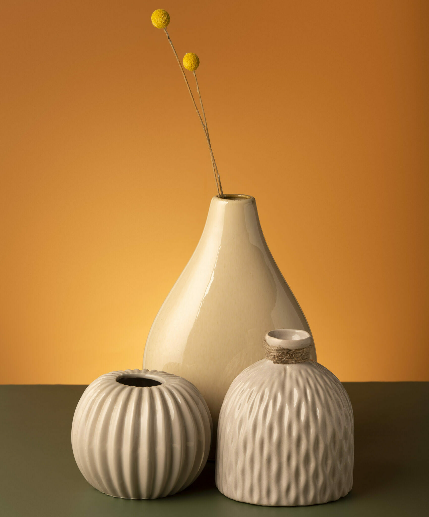 3 vases marrons/beiges sur un meuble gris devant un mur orange